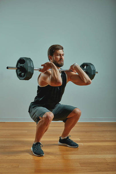 Portrait of super fit muscular young man working out in gym with barbell on gray background, copyspace. - Valokuva, kuva