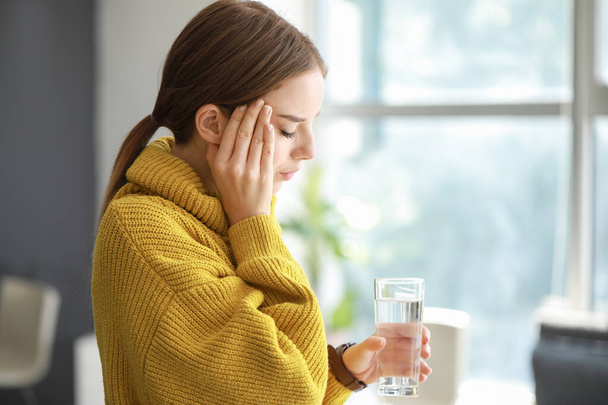 junge Frau mit Glas Wasser leidet zu Hause unter Kopfschmerzen - Foto, Bild