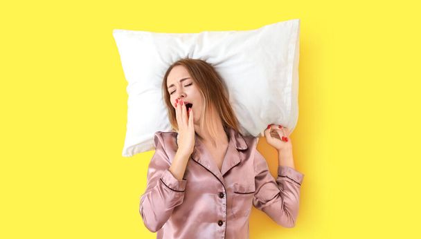 Sleepy young woman with pillow on color background - 写真・画像