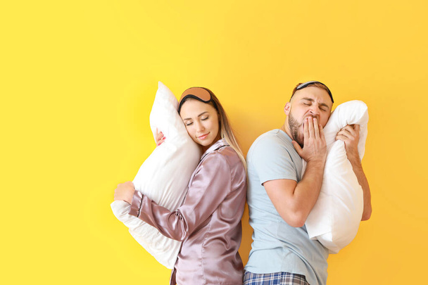 Νυσταγμένο νεαρό ζευγάρι με μαξιλάρια στο φόντο χρώμα - Φωτογραφία, εικόνα