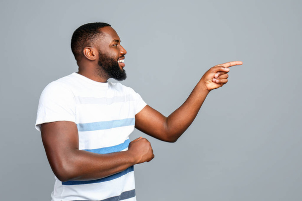 glücklicher afrikanisch-amerikanischer Mann zeigt auf etwas auf grauem Hintergrund - Foto, Bild