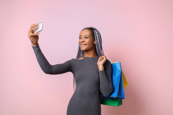 African-American woman with shopping bags taking selfie on color background - Photo, Image
