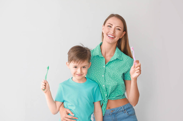 Porträt der Mutter und ihres kleinen Sohnes beim Zähneputzen auf hellem Hintergrund - Foto, Bild