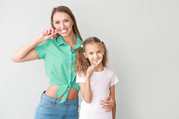 Portrait of mother and her little daughter brushing teeth on light background - Foto, Bild