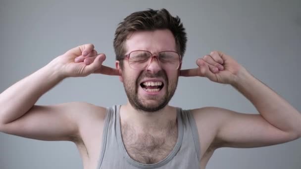 junger Mann mit riesiger Brille, die Ohren geschlossen, die Finger genervt von lauten Geräuschen oder Musik - Filmmaterial, Video