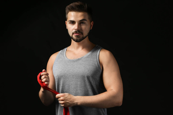 Sporty young man applying wrist bands against dark background - 写真・画像