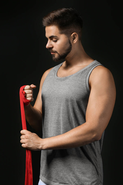 Sporty young man applying wrist bands against dark background - Foto, immagini