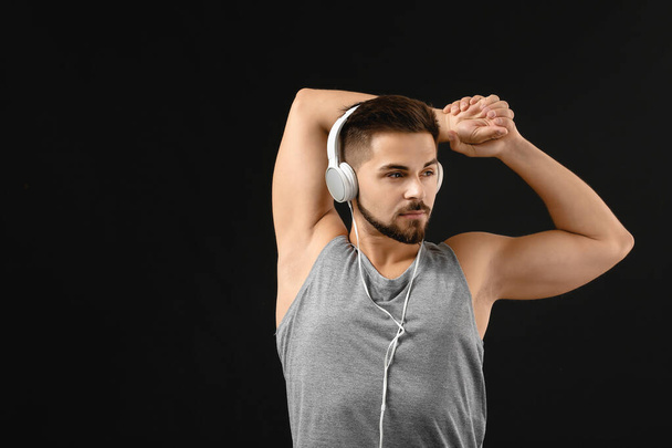 Sporty young man listening to music and training against dark background - Фото, изображение