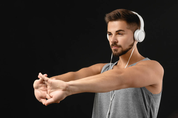 Sporty young man listening to music and training against dark background - Photo, Image