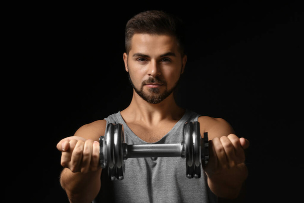 Sporty young man with dumbbell on dark background - Fotoğraf, Görsel