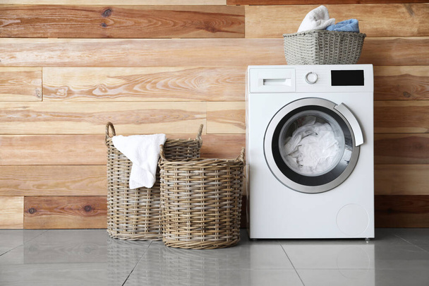 Moderne wasmachine met wasruimte in de buurt van houten muur - Foto, afbeelding