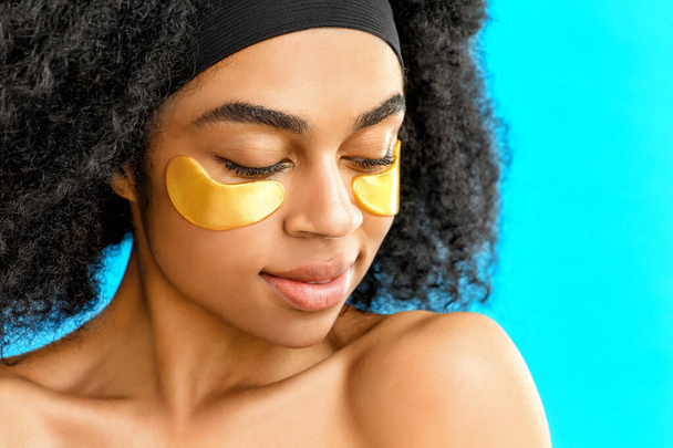 Portrait of beautiful African-American woman with under-eye patches on color background - Photo, Image