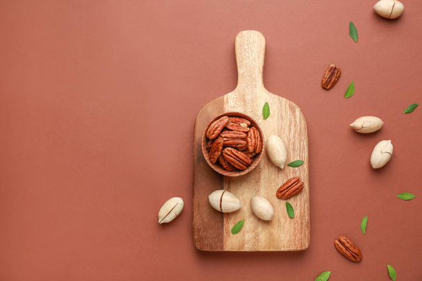 Board with tasty pecan nuts on color background - Фото, изображение