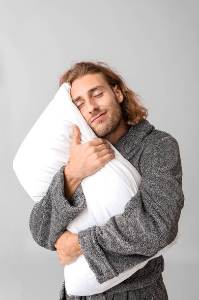 Porträt eines verschlafenen Mannes im Bademantel und mit Kissen auf grauem Hintergrund - Foto, Bild