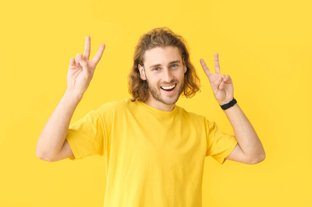 Portrait of happy man showing victory gesture on color background - Photo, Image