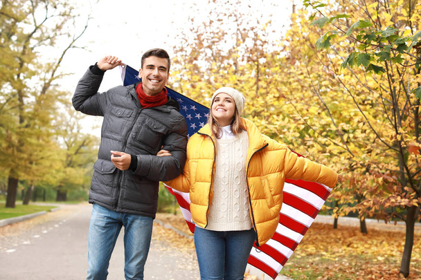 Jovem casal com bandeira dos EUA no parque de outono
 - Foto, Imagem