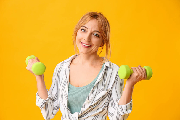 Portrait of mature woman with dumbbells on color background - Valokuva, kuva