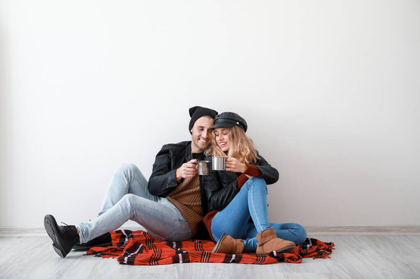 Heureux jeune couple dans des vêtements chauds d'automne boire une boisson chaude tout en étant assis près du mur blanc
 - Photo, image
