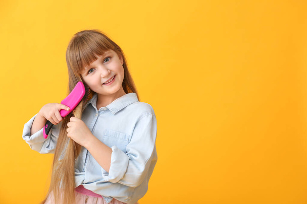 Cute little girl brushing hair on color background - Photo, Image
