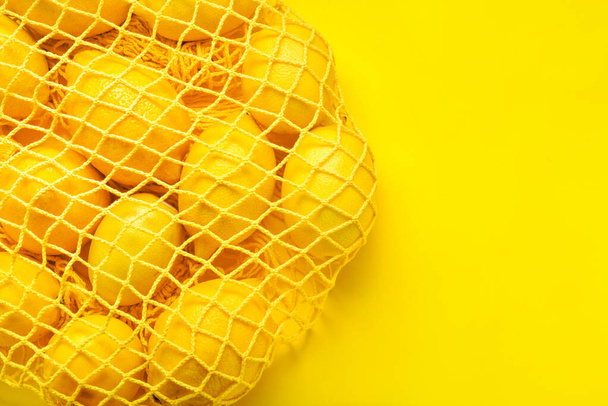 Сетчатый мешок с созревшими лимонами на цветном фоне
 - Фото, изображение