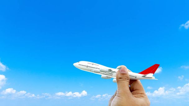 Молодой азиат держит в руках миниатюрный игрушечный самолет, летящий на голубом небе на фоне заката. Путешествие и поездка летом на самолете с копировальным пространством
 - Фото, изображение