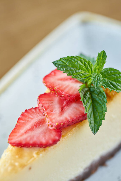 Primer plano de delicioso pastel de queso con hojas de fresa y menta en un plato blanco
. - Foto, Imagen