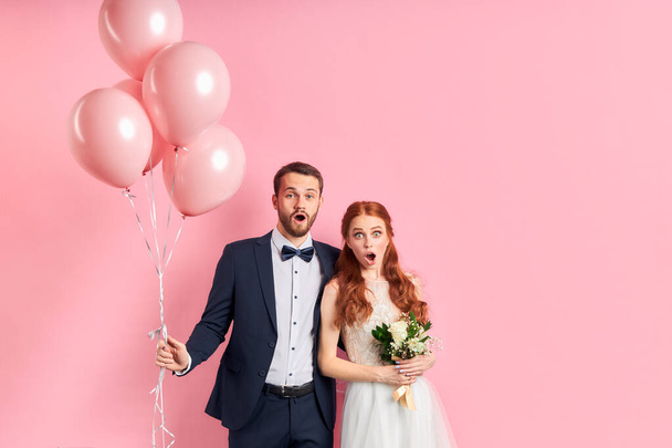 Portrait of surprised young wedding couple standing isolated over pink background - Foto, afbeelding