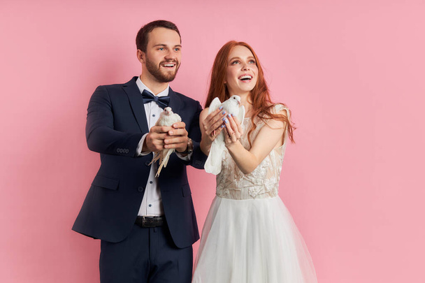 Smiling man and woman holding pigeons in hands isolated over pink background - Φωτογραφία, εικόνα