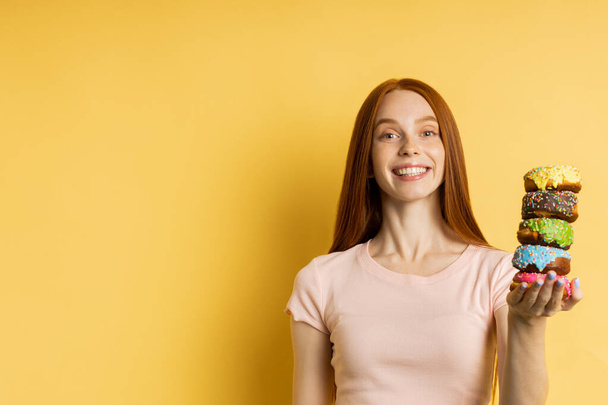 Young beautiful woman with doughnuts on yellow background - Fotoğraf, Görsel