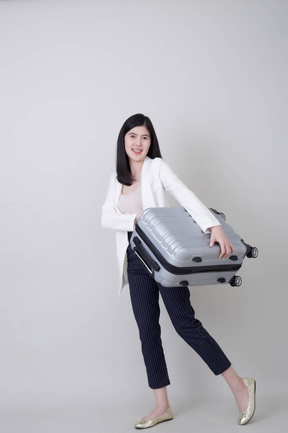 Красива молода азіатка-туристка посміхається і тягне сірий кольоровий багаж, щоб подорожувати на своїй відпустці ізольовано на світло-сірому банерному фоні студії з копіювальним простором
 - Фото, зображення