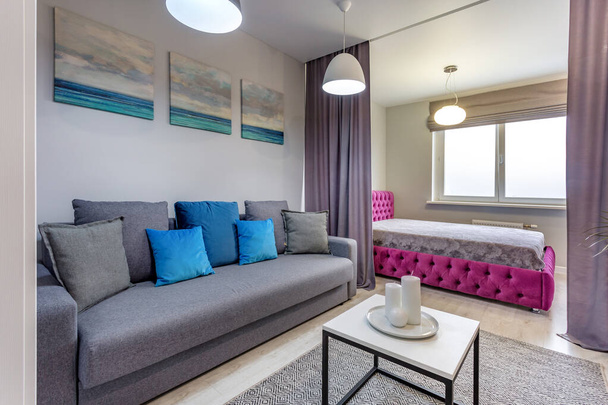 MINSK, BELARUS - SEPTEMBER, 2019: Interior of the modern bedroom in studio apartments with double bed, sofa and blue pillows - Zdjęcie, obraz