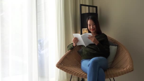 πλάνα από όμορφη Ασιάτισσα γυναίκα ανάγνωση βιβλίο στον καναπέ στο σπίτι - Πλάνα, βίντεο