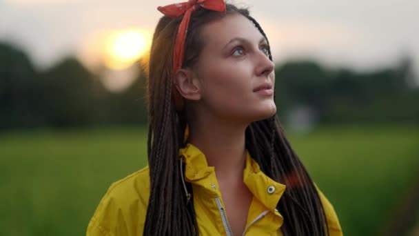close-up portret van jonge vrouw glimlachend in de wind kijkend naar zonsondergang boven bos - Video
