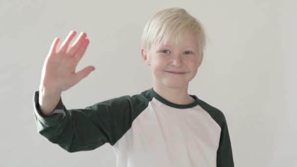 Niño rubio agitó su mano en el estudio sobre un fondo blanco
 - Metraje, vídeo