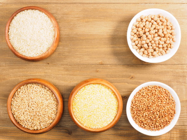 Rice, oat, buckwheat, corn flakes, chick pea in cups on brown wo - Foto, afbeelding