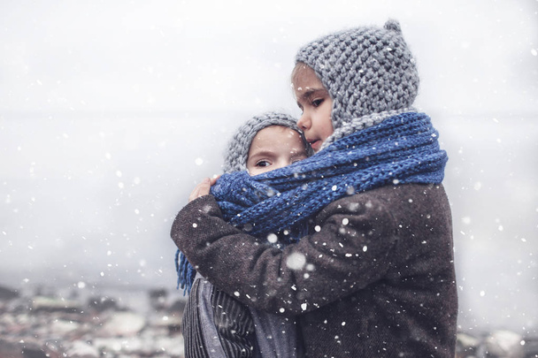 Girl in knitted grey hat hugging her frozen smaller brother - Photo, Image