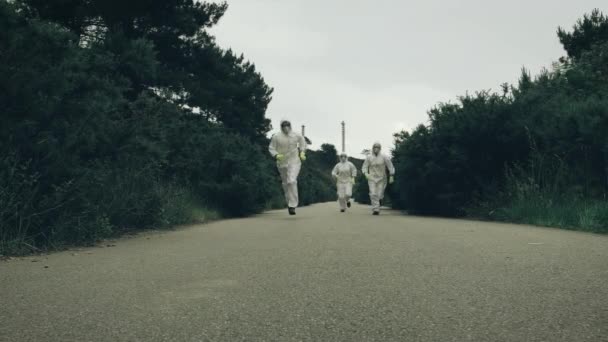 Mensen met bacteriologische beschermingspakken die weglopen op een eenzame weg - Video