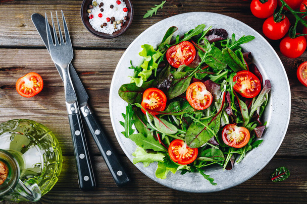 Mistura de folhas frescas de salada verde com rúcula, alface, espinafre, beterraba e tomate sobre fundo rústico de madeira
. - Foto, Imagem