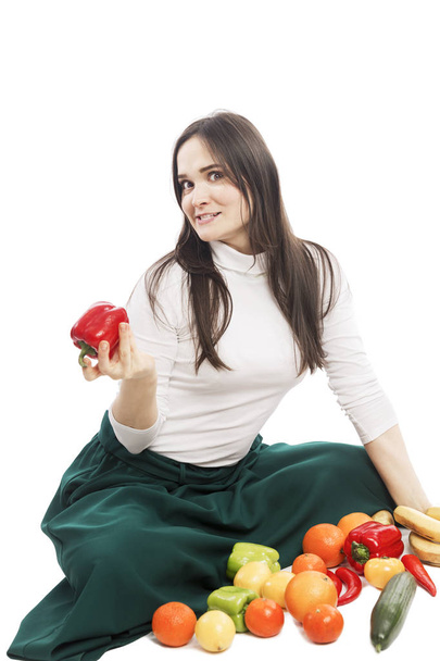 Nuori hymyilevä naispuolinen kasvissyöjä istuu erilaisten vihannesten ja hedelmien vieressä. Eristetty valkoisella pohjalla
.  - Valokuva, kuva