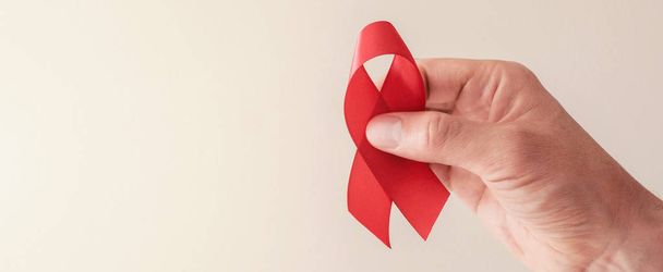 Hands holding red ribbon on red background, hiv awareness concep - Фото, зображення
