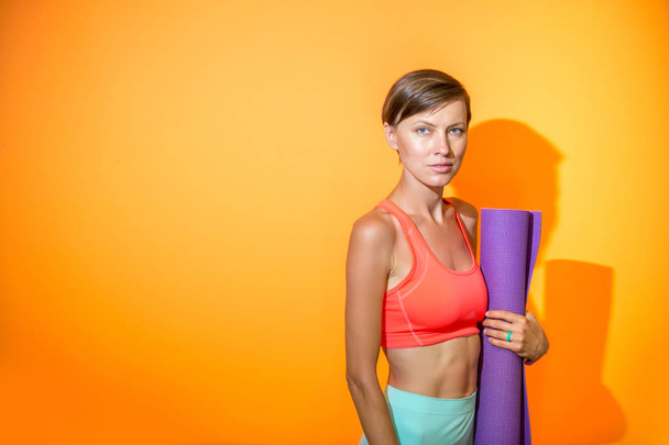Sporty yoga girl with yoga mat isolated over yellow orange background, copy space - Zdjęcie, obraz