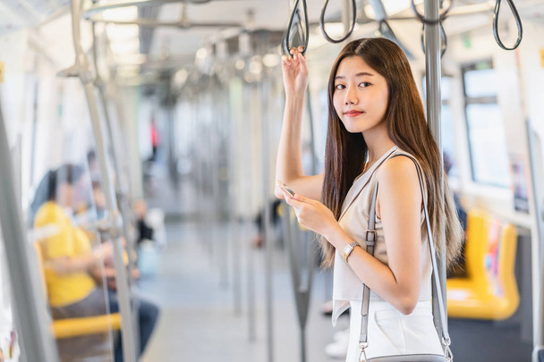 Молода азіатка жінка-пасажирка, яка користується соціальною мережею через розумні мобільні телефони в поїзді метро під час подорожей у великому місті, японці, китайці, корейці і повсякденному житті, приміські та транспортні концепції - Фото, зображення