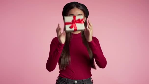 Cute european young woman with red lips holding gift box with bow on pink wall background. Girl smiling, she is happy to get present. - Filmati, video