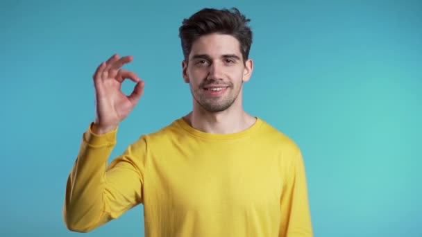 Positive young man smiles to camera. Hipster guy showing OK sign over blue background. Winner. Success. Body language. - Footage, Video