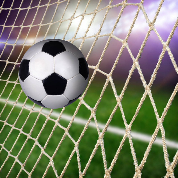 Μπάλα στο δίχτυ γκολ με πράσινο γήπεδο ποδοσφαίρου και φως σε σκούρο φόντο - Φωτογραφία, εικόνα
