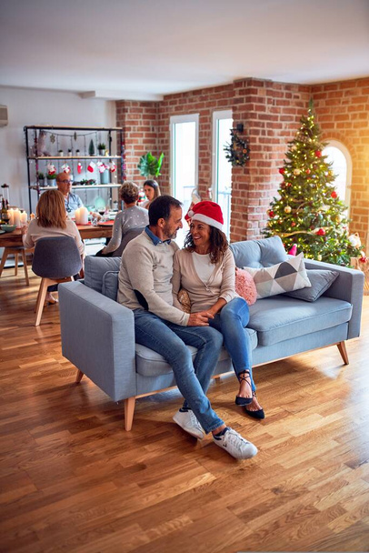 Семья и друзья ужинают дома в канун Рождества с традиционной едой и украшением, романтическая старшая пара разговаривает вместе сидя на диване
 - Фото, изображение
