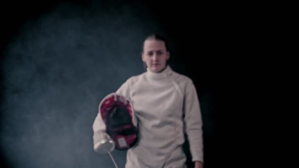 Miekkailukoulutus - nuori naismiekkailija kävelee ulos pimeästä ja laittaa suojakypärän päähän - asettuu paikoilleen ja alkaa taistella
 - Materiaali, video