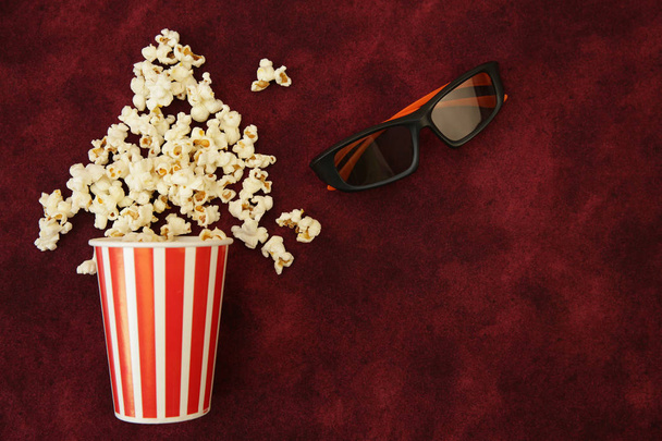 popcorn in a paper Cup and popcorn flies out with movie glasses on a red background with space for text. Flat Lay, Top View. Background, pattern, card. The concept of cinema. - Foto, imagen