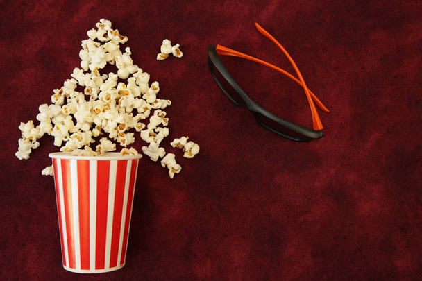 popcorn in a paper Cup and popcorn flies out with movie glasses on a red background with space for text. Flat Lay, Top View. Background, pattern, card. The concept of cinema. - Фото, изображение