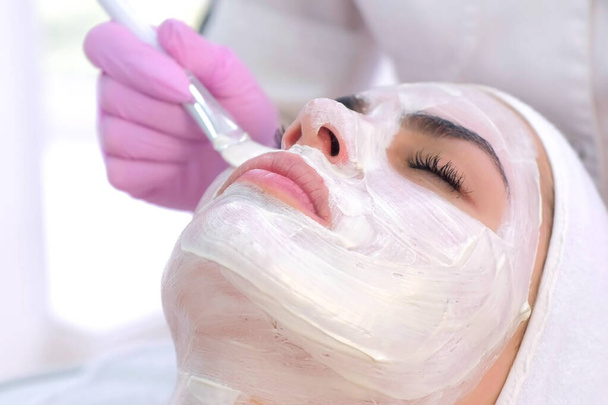 Cosmetologist is applying white mask on woman client face in beauty clinic. - Foto, immagini